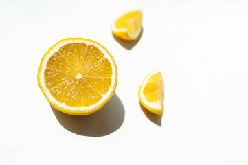 half a juicy ripe yellow lemon and two small slices on a white background with hard shadows in natural light