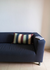Sofa in dark blue with a colorful striped throw pillow and a book on the arm.  In a white paint wall room.
