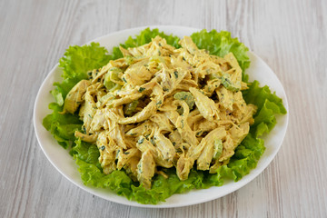 Homemade Coronation Chicken Salad on a white plate on a white wooden surface, low angle view.