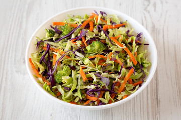 Homemade Raw Shredded Broccoli Slaw in a white bowl on a white wooden background, side view.