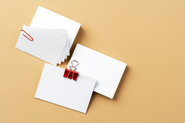 Pile of white businesscards with a clip on beige background, copy space
