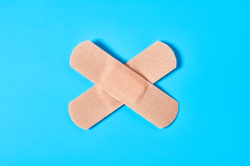 Sticky medical patch in form of cross on blue background. Healthcare concept