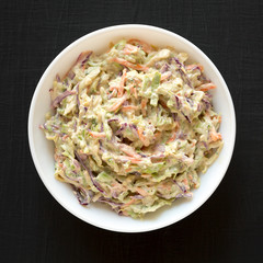 Homemade Creamy Broccoli Slaw in a white bowl on a black surface, top view. Flat lay, from above, overhead.