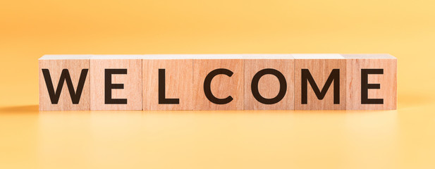 Word WELCOME written on wooden cubes on yellow background.