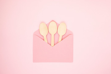 Eco-friendly biodegradable compostable wooden spoons in a pink envelope on a soft pink background. Alternative to a disposable plastic spoon