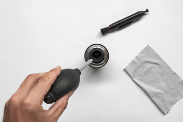 Camera lens cleaning with a air blower on white background. Hand with air blower, lens and set of air blower, microfiber cleaning cloth and lens cleaner brush for removes dust and dirt from lens.
