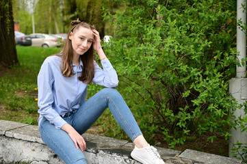 Model posing sitting in spring park outdoors in the city. Photo of a young pretty girl with a smile...