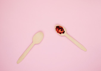 Eco-friendly biodegradable compostable wooden spoons on a soft pink background. Red confetti hearts on spoons. Background for the holidays