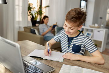 Fototapeta premium children, education and learning concept - happy smiling student boy with book writing to notebook at home