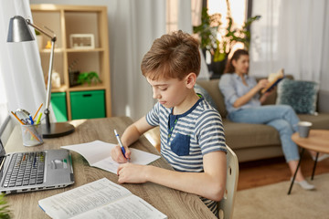 children, education and learning concept - happy student boy with book writing to notebook at home