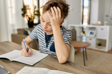 children, education and learning concept - student boy with book writing to notebook at home