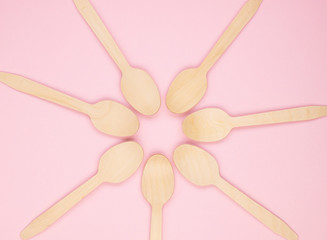 Eco-friendly biodegradable compostable wooden spoons on a soft pink background. Wooden spoons are gathered together in the center. Background for the holidays