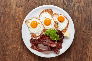 3 Spiegeleier mit Speck gebraten auf einem weißem Teller und Holztisch
