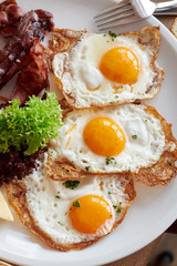 3 Spiegeleier mit Speck gebraten auf einem weißem Teller und Holztisch