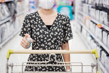 Asian woman cleaning surface of shopping cart by alcohol spray in supermarket or grocery, protect...