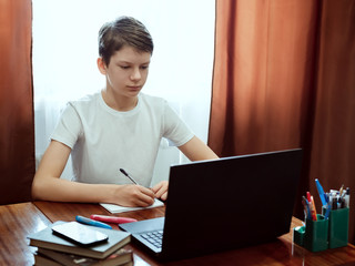 Student looking at computer, watching online education classes or webinar at home. Schoolboy studying with laptop and doing school homework. Distance and e-learning education concept, online lessons