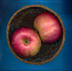 Fresh ripe red apples in a basket on a blue background. Top view.