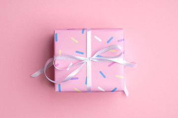 Square gift box wrapped pink paper with confetti and ribbon bow on pink background top view