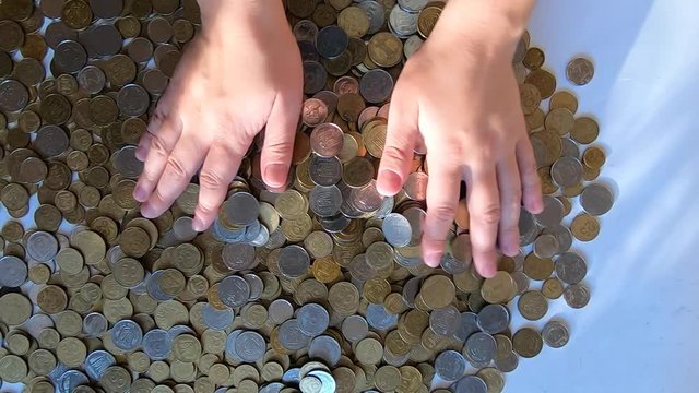 Person two hands rakes coins on table, pours spills from handful to surface