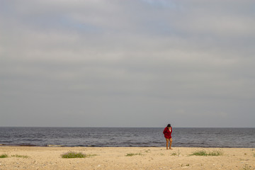A lonely woman in red is walking on a sandy beach and looking for something