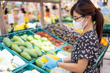 Asian woman wearing nitrile gloves and holding ripe mango fruit in supermarket or grocery, protect coronavirus inflection. Hygiene, new normal and life after covid-19 pandemic