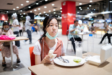 Fototapeta premium Social distancing,asian child girl is eating at a food court after Coronavirus quarantine or Covid-19,department store allow people to sit and eat by separating the tables and keeping distance,safety