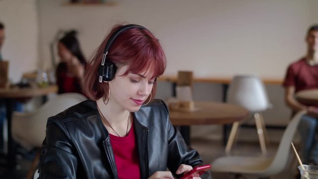 Young woman sitting in cafe, using headphones and smartphone. Slow motion.