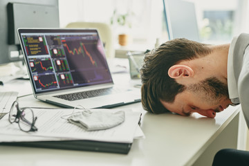 Frustrated young manager banging his head on table after financial analysis of company budget,...