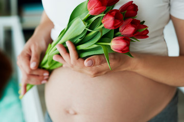 Obraz na płótnie Canvas Close up of human pregnant abdomen and bunch of flowers