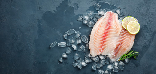 Fresh fish fillet of sea bass in ice on a dark slate background. Top view. Copy space for text. - obrazy, fototapety, plakaty