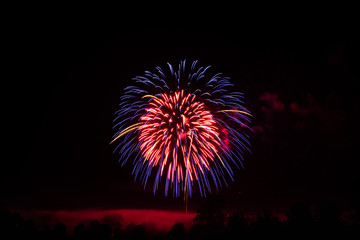 Fireworks lighting up low hanging smoke, silhouetting some trees