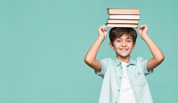 Smiling boy holding stack of books on head