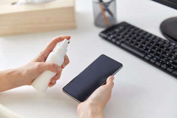 hygiene, cleaning and disinfection concept - close up of woman hands spraying hand sanitizer to smartphone