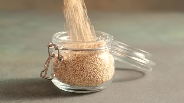 White raw quinoa, South American grain, female hands pour seeds into glass jar. Healthy and gluten free food.