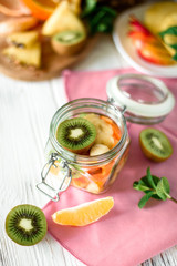 Top view of serving food in a glass jar with sliced fruits on a pink overlay and wooden table