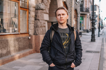 A young man in a jacket walks through the streets of the city, portrait against the background of a beautiful old building, business style