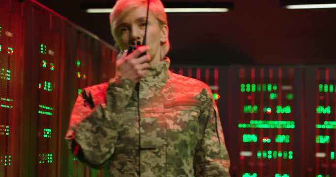 Alert signals red lights in server room. Caucasian woman walking and talking in walkie-talkie while evacuating from data center. Emergency situation concept Danger alarm Military evacuation Red lights