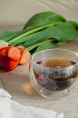 a clear glass cup of hot tea on the table, next to a bouquet of tulips. spring tea party. authentic image