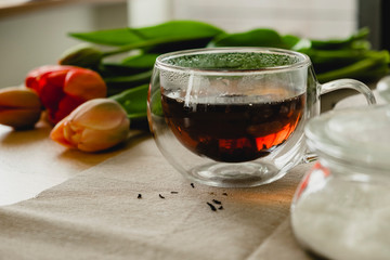 a clear glass cup with hot black tea, a bouquet of red tulips are on the table. spring tea party