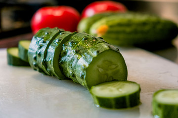 a fresh green cucumber cut into slices lies on a light cutting board. in the background -...