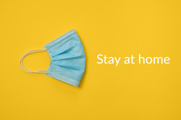 COVID-19 disposable surgical face mask on yellow background. Protection against coronavirus and epidemic. Medical concept with "stay at home" text