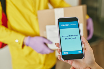 Close-up of unrecognizable customer using online banking app while paying for delivery with smartphone