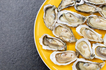 Fresh oysters ready to be eaten raw. Oysters on a yellow plate and a black stone. Raw fish with oysters, luxurious dinner and quality fresh shellfish.  Restaurant special dish