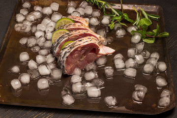 Fresh river fish on metal tray with melting ice. Lemon and sprigs of rosemary.