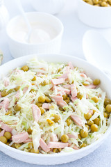 vegetable salad with cabbage, sausages and canned peas on a white plate, selective focus