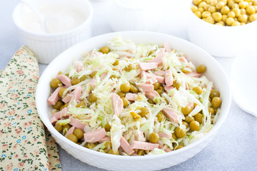 vegetable salad with cabbage, sausages and canned peas on a white plate, selective focus
