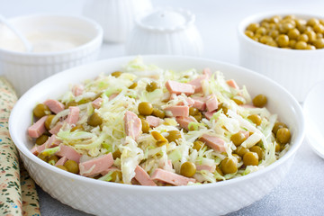 vegetable salad with cabbage, sausages and canned peas on a white plate, selective focus