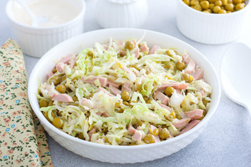 vegetable salad with cabbage, sausages and canned peas on a white plate, selective focus