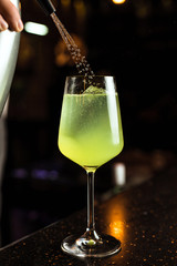 Bartender prepairing a green cocktail with ice in a wine glass, adding soda water