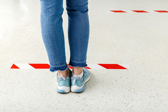 People Stand In Line Keeping Social Distance, Woman Standing Behind A Warning Line During Covid 19 Coronavirus Quarantine. Safe Shopping, Social Distancing Concept. Legs In Line Close Up